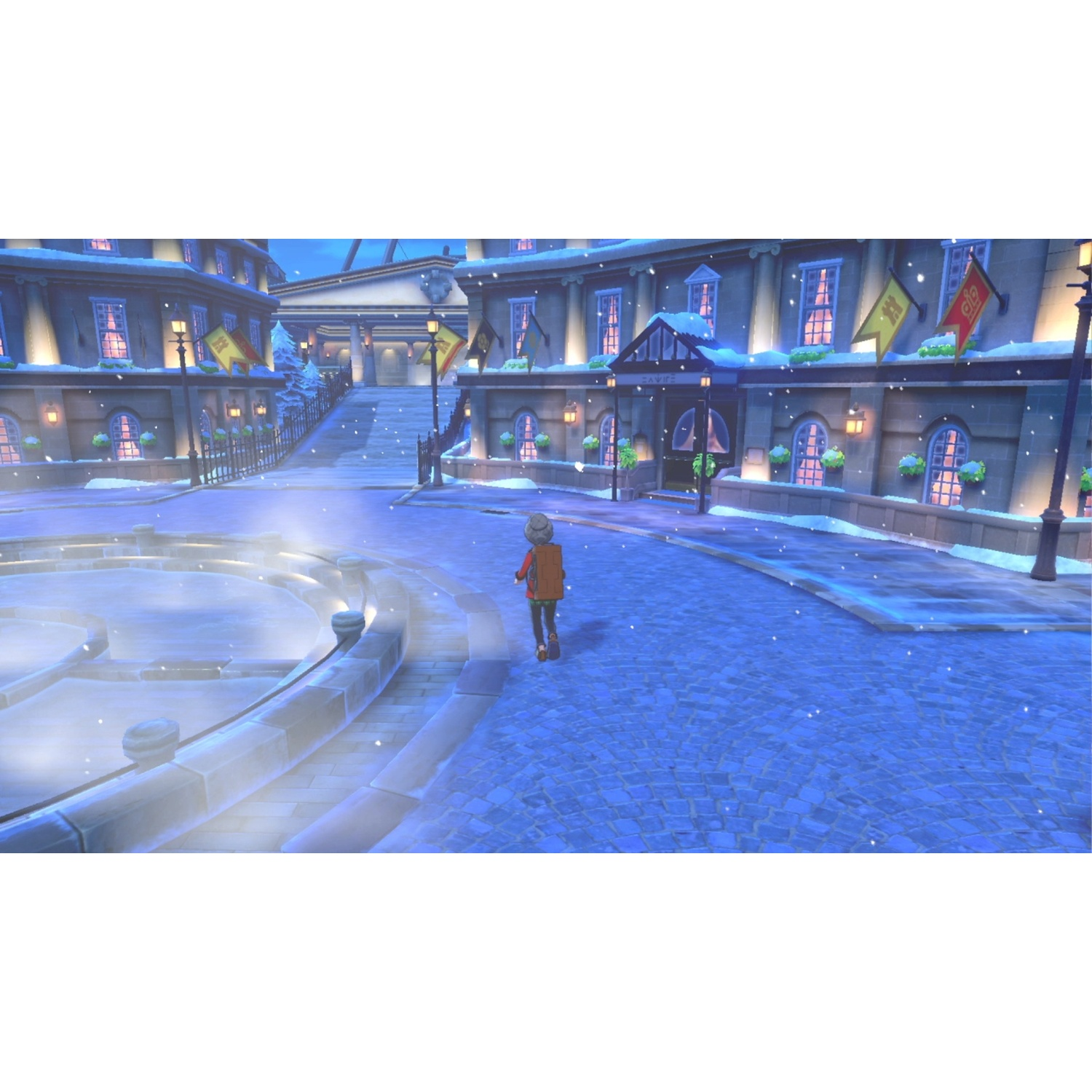 A person walks on a snowy street past buildings with flags. A fountain is on the left.