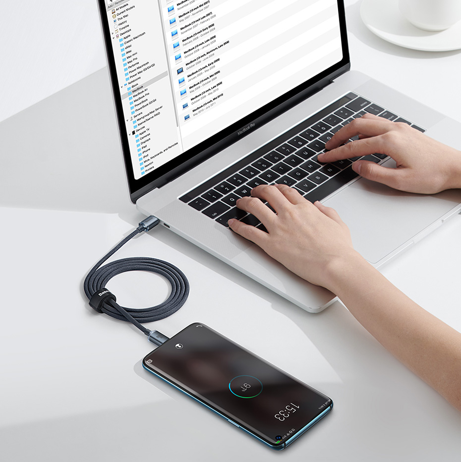 Una persona escribe en un MacBook Pro mientras un smartphone está conectado por cable.