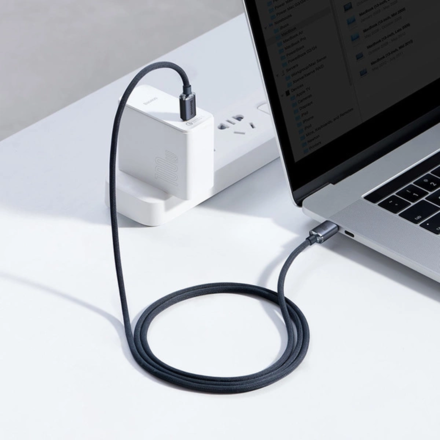 Un cargador blanco de 100W con cable negro carga un portátil.