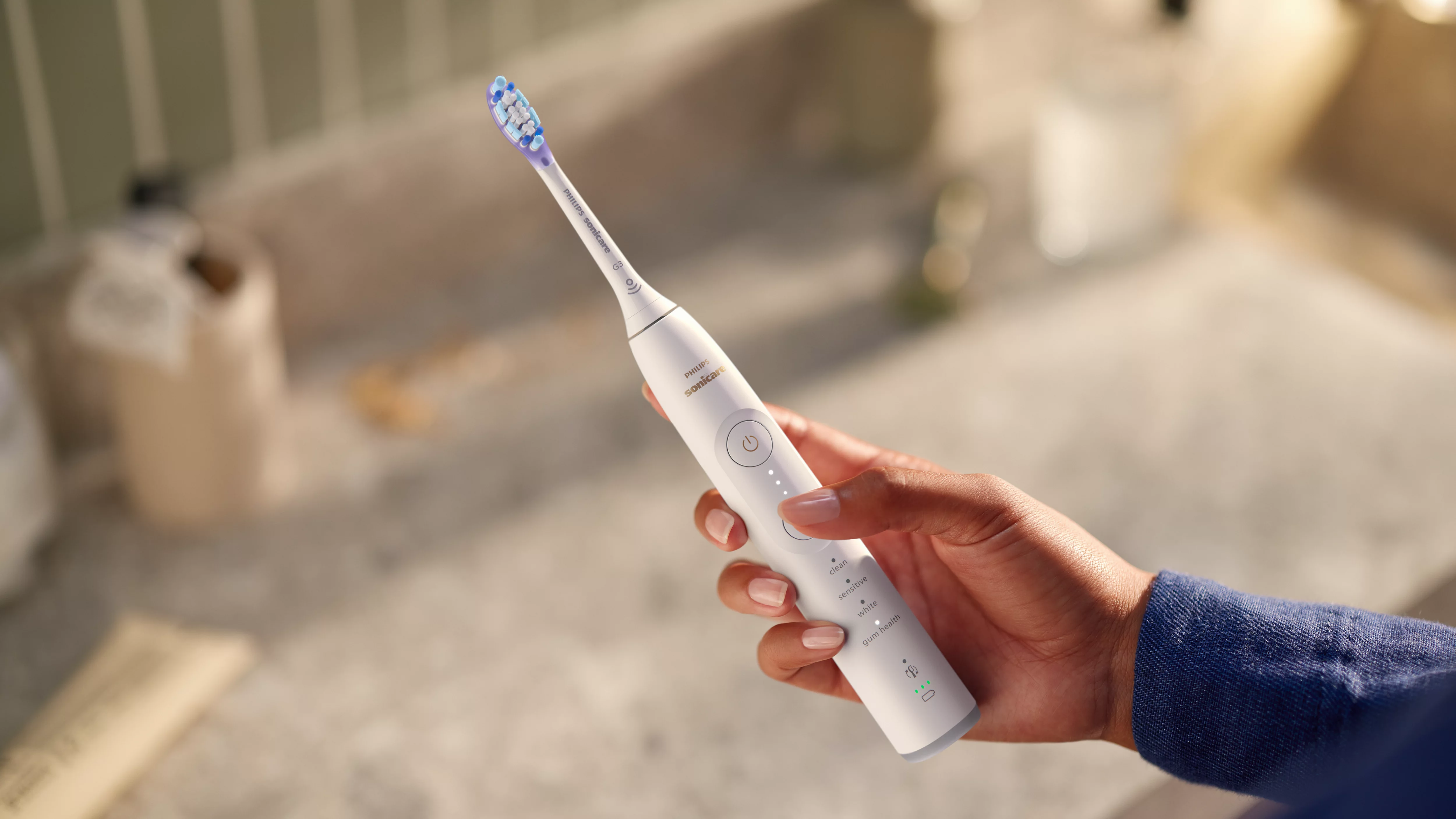 Eine Hand hält eine weiße elektrische Zahnbürste mit blauen und weißen Borsten.