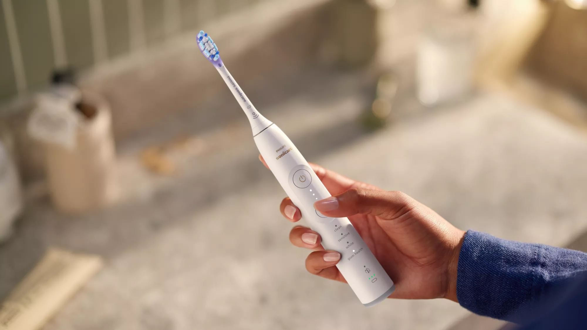 Eine Hand hält eine weiße elektrische Zahnbürste mit blau-weißen Borsten.