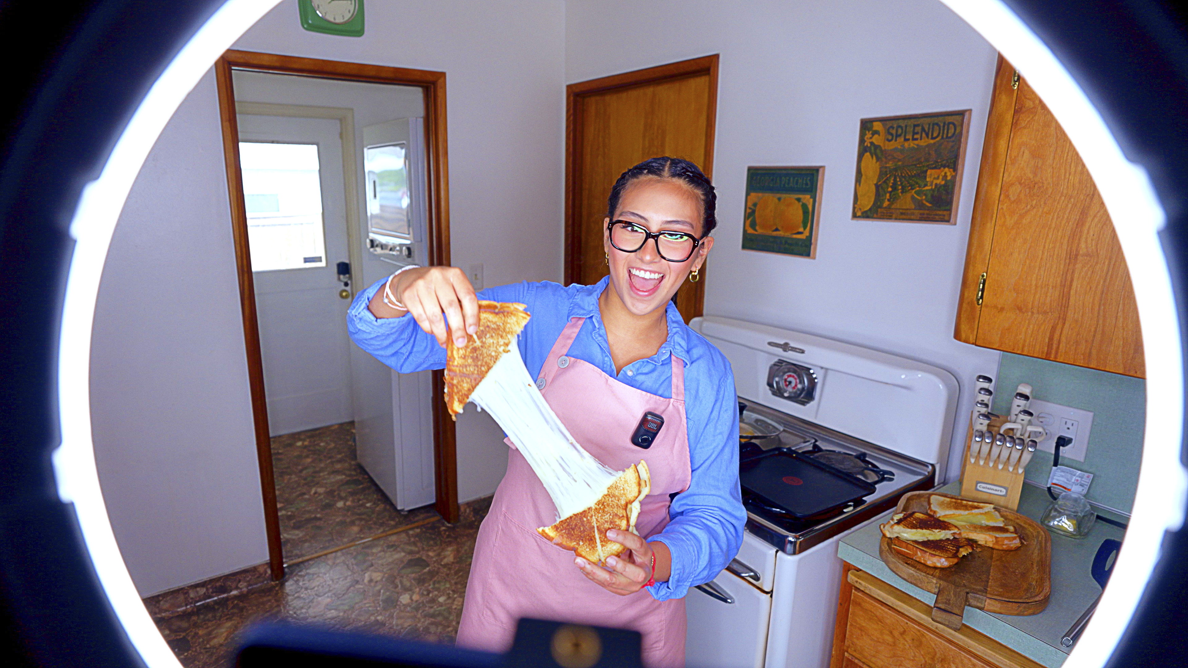 Eine Frau in einer Schürze hält einen Käsesandwich mit dehnbarem Käse hoch.