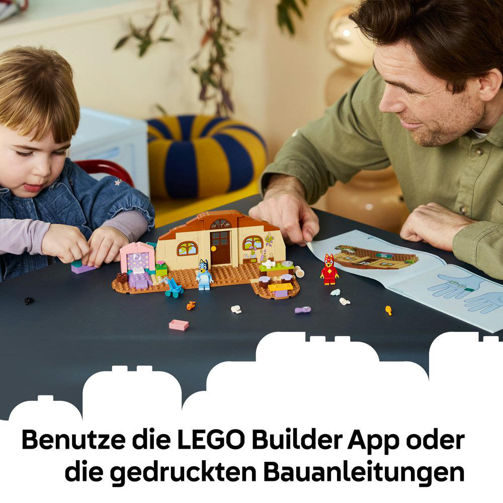 Vater und Kind bauen Lego mit Anleitung. Ein Haus und Figuren sind auf dem Tisch.