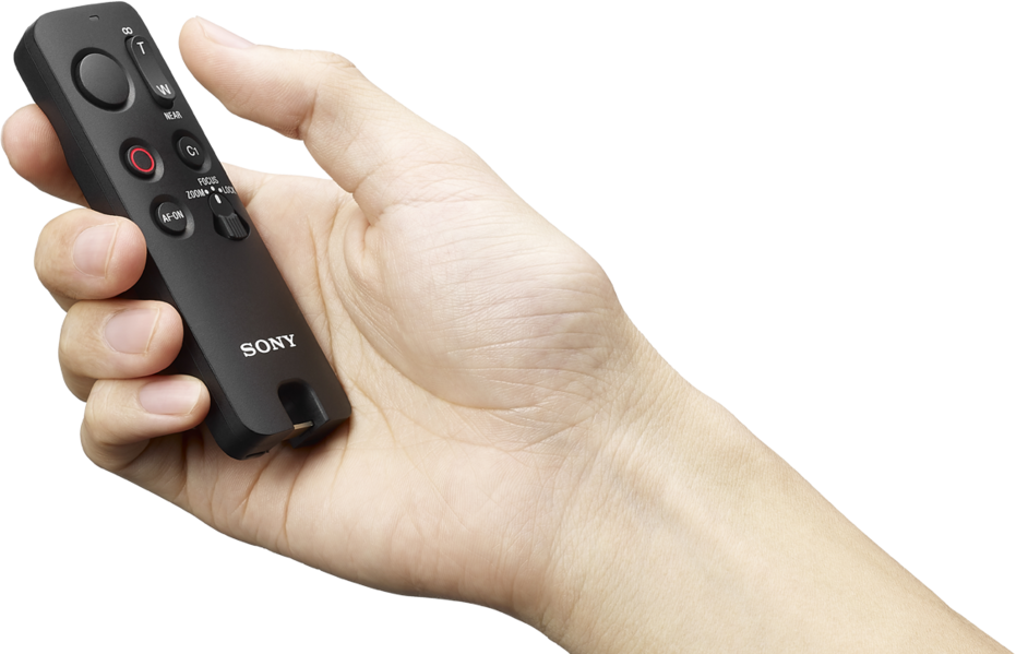 Una mano tiene un telecomando Sony nero con pulsanti zoom, messa a fuoco e registrazione.