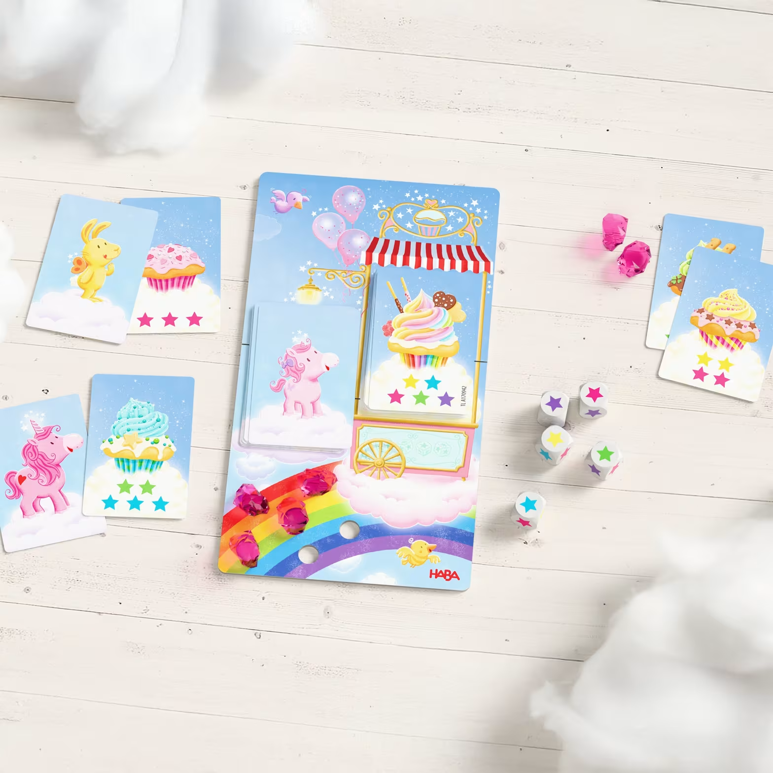 Egy társasjáték egyszarvúkkal, cupcake-ekkel és szivárvánnyal faasztalon.