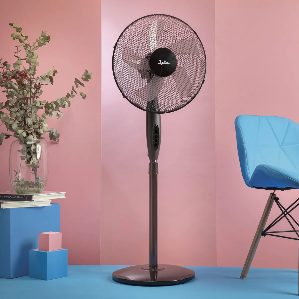 Un ventilador de pie oscuro está junto a una silla azul sobre suelo azul.