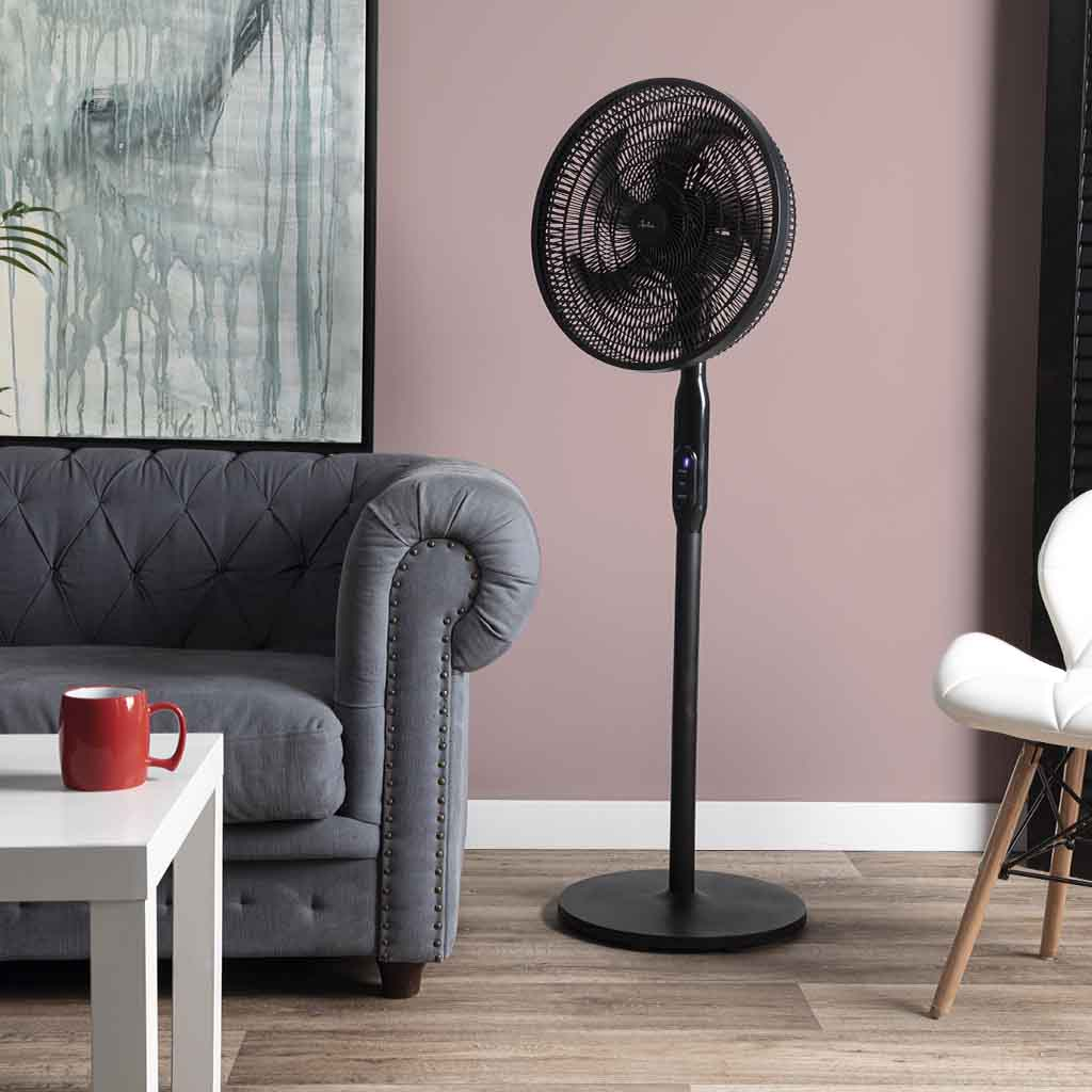 Un ventilador de pie negro está junto a un sofá gris y una mesa blanca.