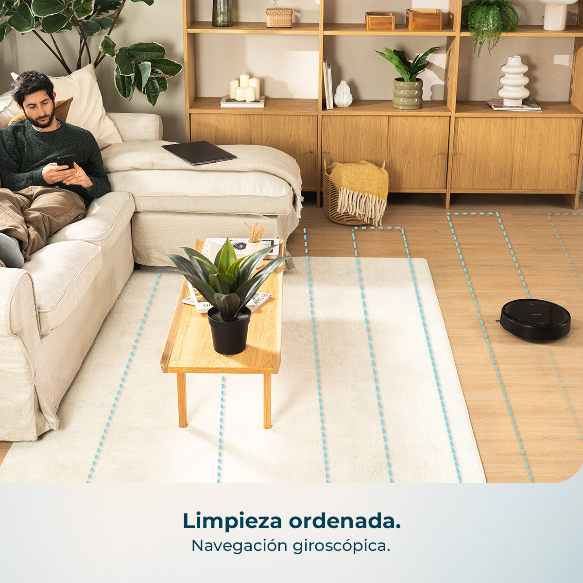 Un hombre se sienta en un sofá usando su teléfono. Un robot aspirador limpia el suelo.