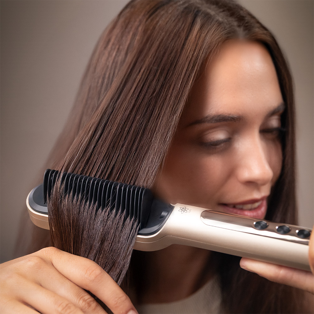 Una mujer se peina el cabello castaño con un peine alisador dorado.