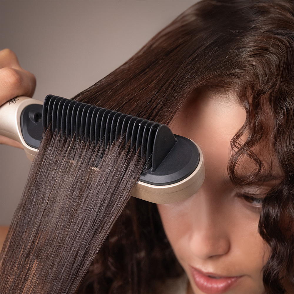 Una persona se alisa el pelo castaño con un peine eléctrico.