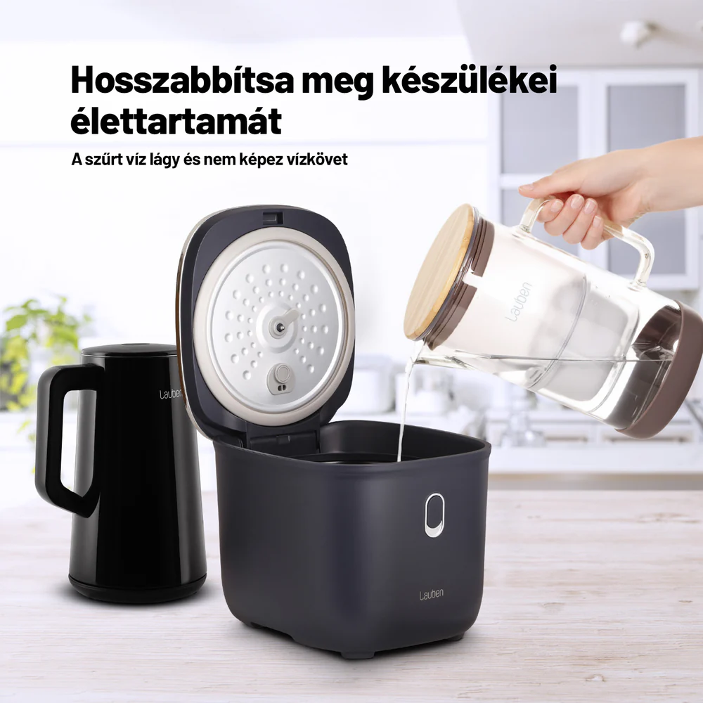 Egy kéz vizet önt ki egy korsóból egy nyitott vízforralóba egy fekete kancsó mellett.