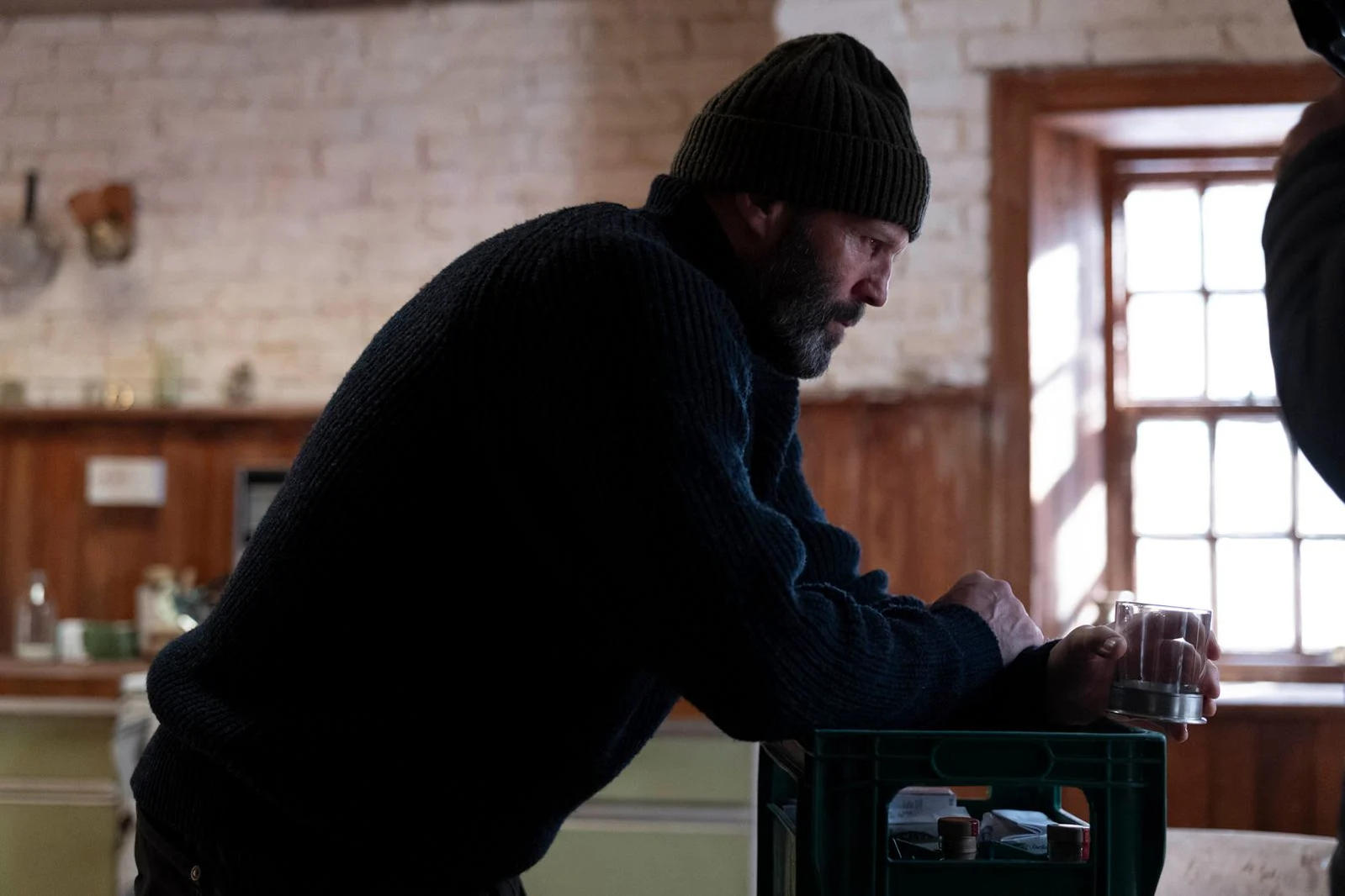 Ein Mann mit Bart trägt eine Mütze und einen Pullover und hält ein Glas.