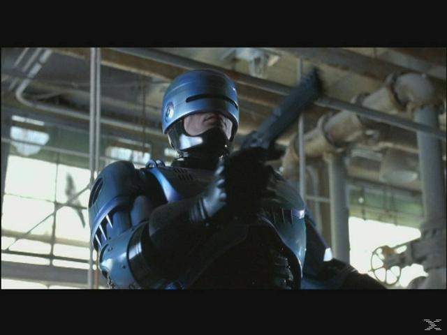 RoboCop in blauer Rüstung hält seine Waffe, industrielle Hintergrundrohre.
