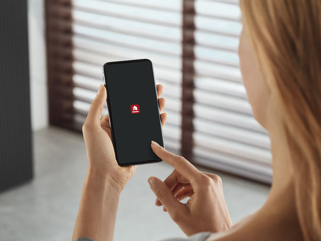 Kobieta trzyma smartfon z logo Miele na ciemnym ekranie.