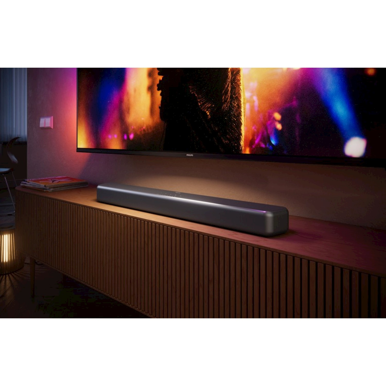 Una soundbar sottile poggia su un mobile in legno davanti a una TV con luci colorate.