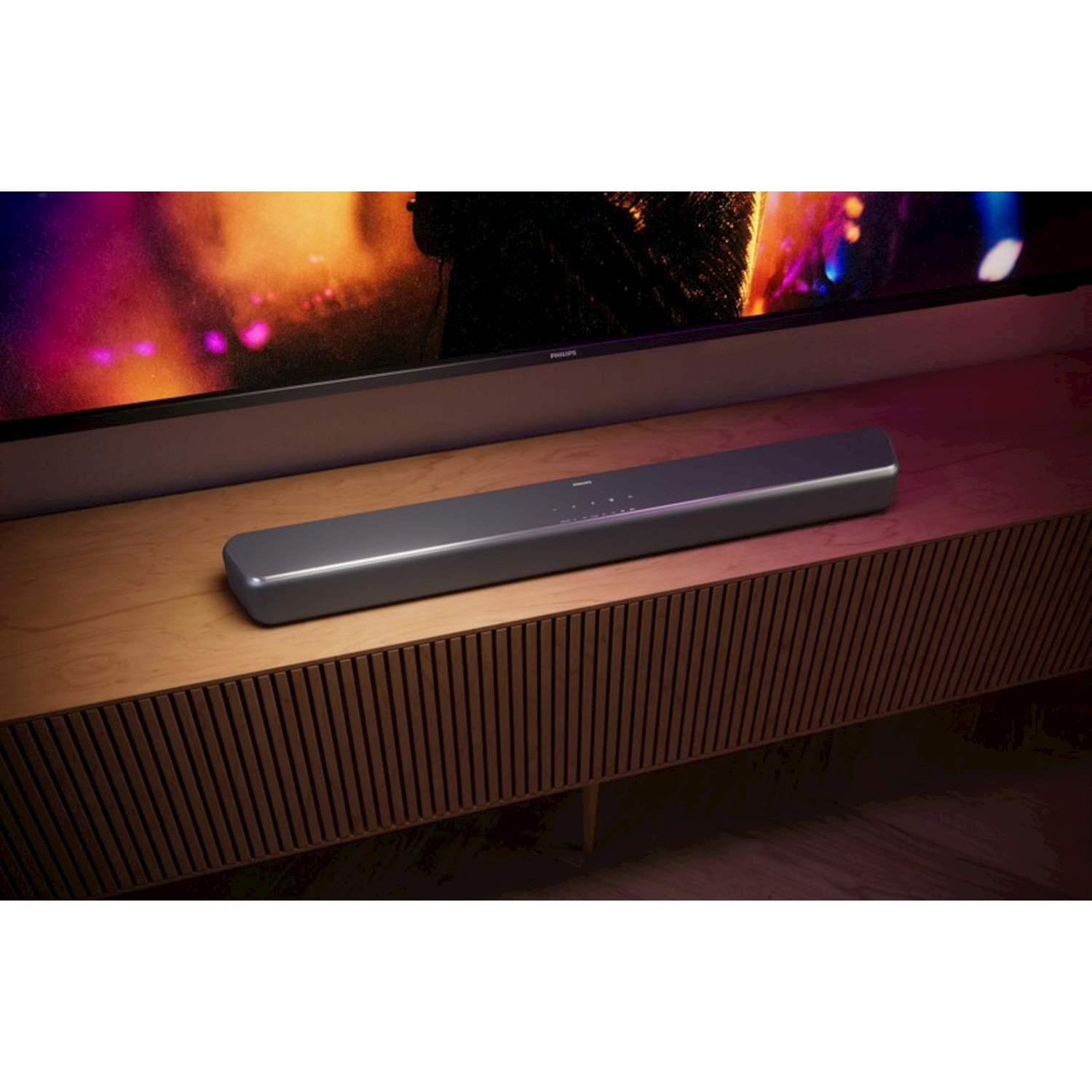 Una soundbar grigia si trova su un mobiletto di legno davanti a una televisione.