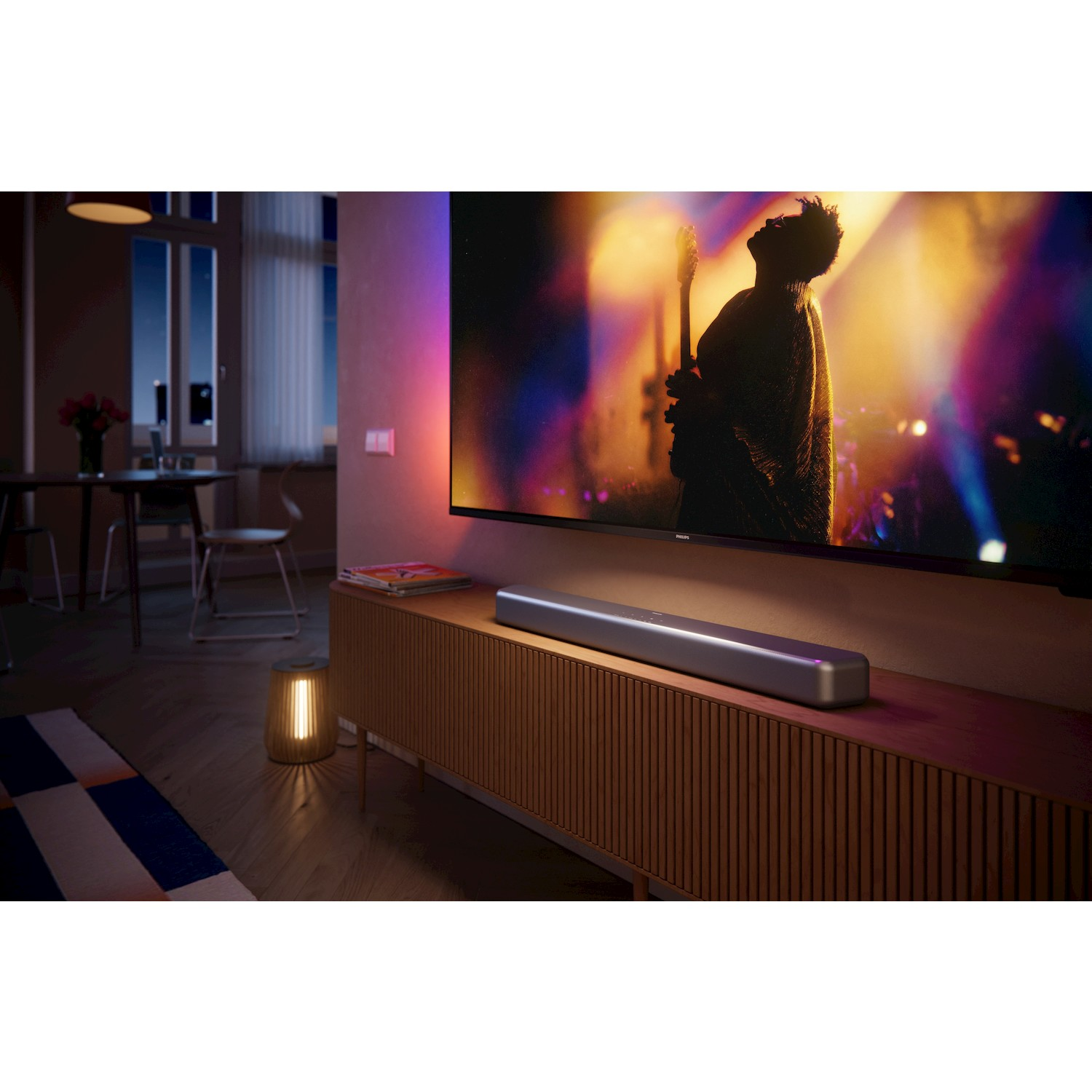 Un uomo con chitarra su schermo, davanti soundbar su mobile legno.