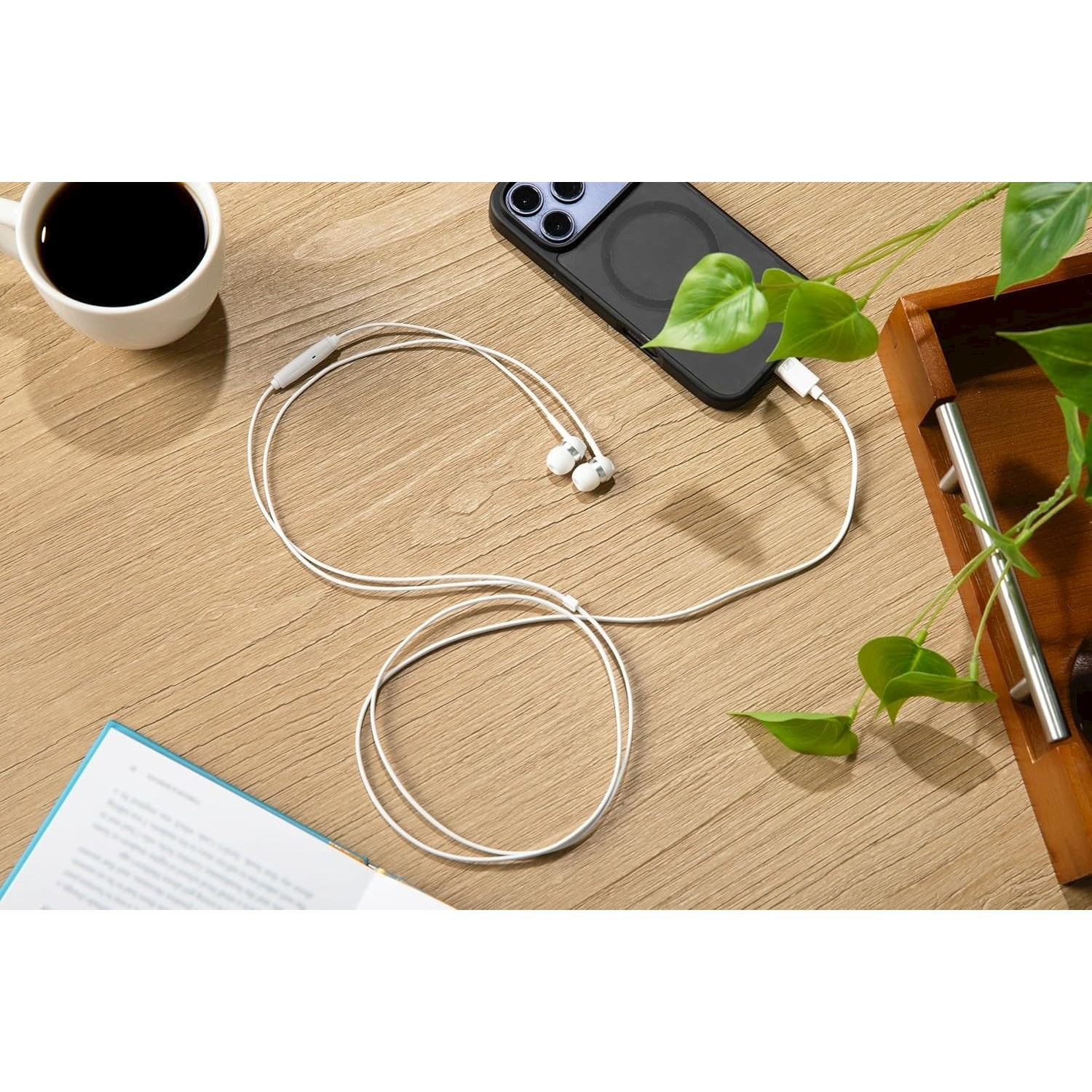 Auricolari accanto a tazza di caffè, telefono e libro su tavolo legno.