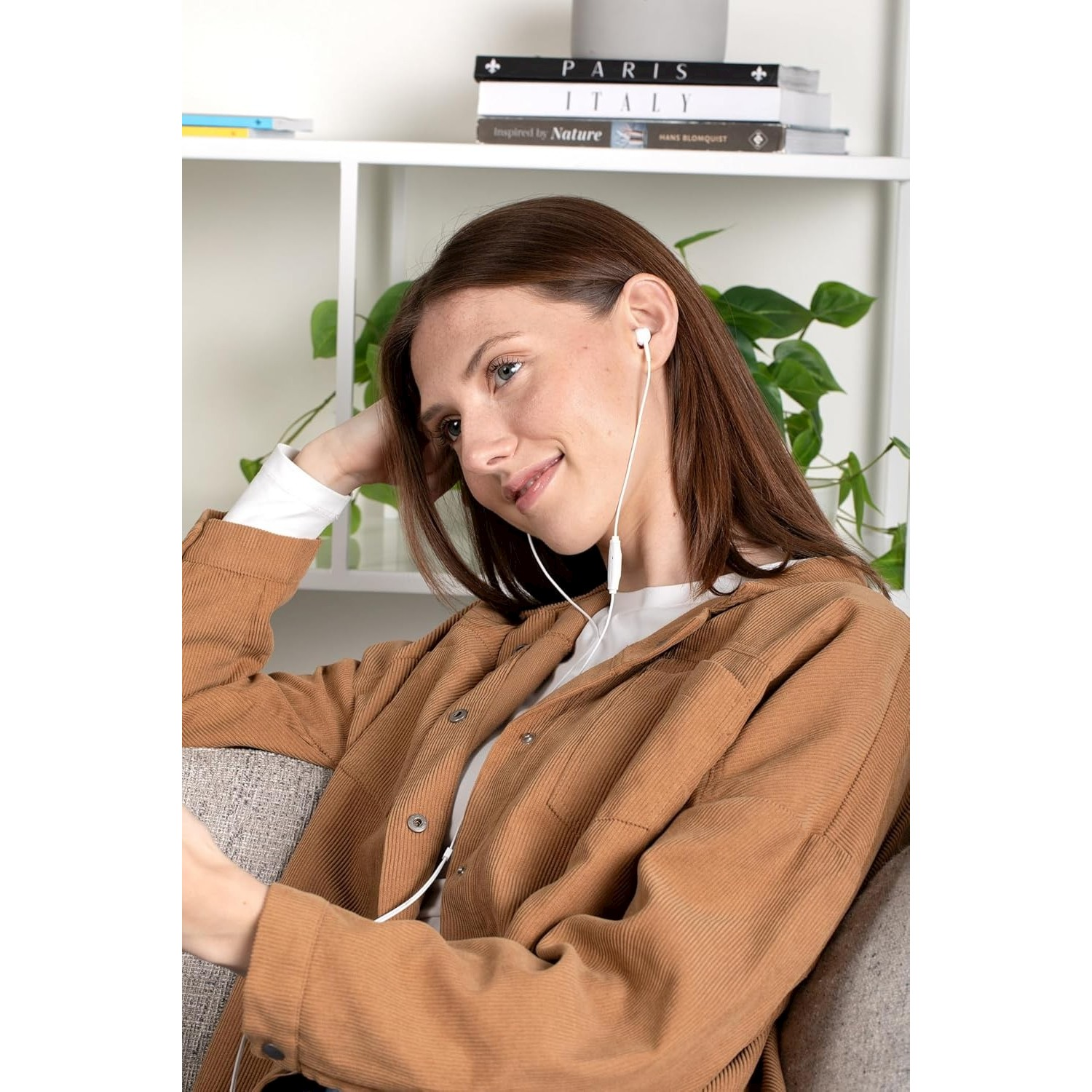 Una donna con auricolari seduta su un divano, guarda in basso.