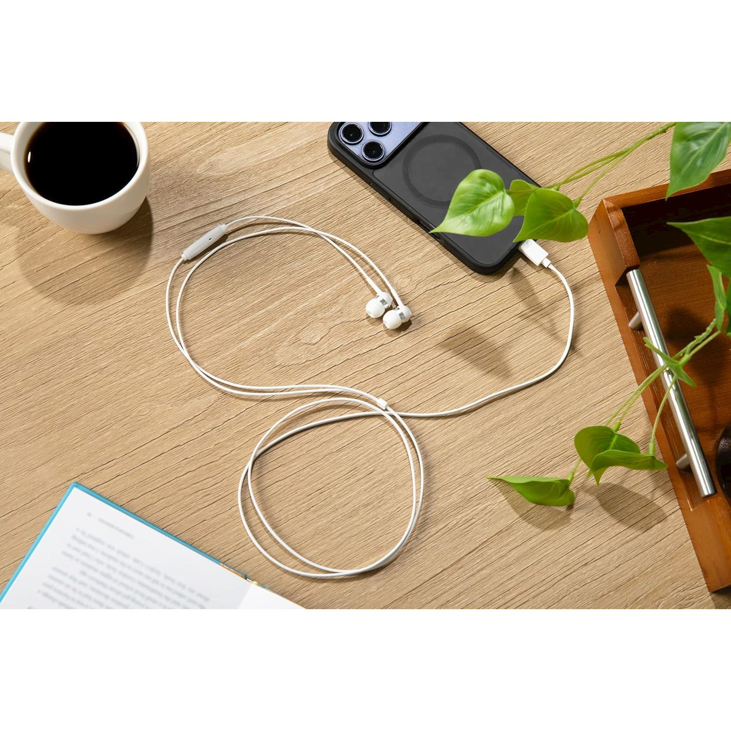 Auricolari bianchi collegati a uno smartphone, accanto a una tazza di caffè e un libro.