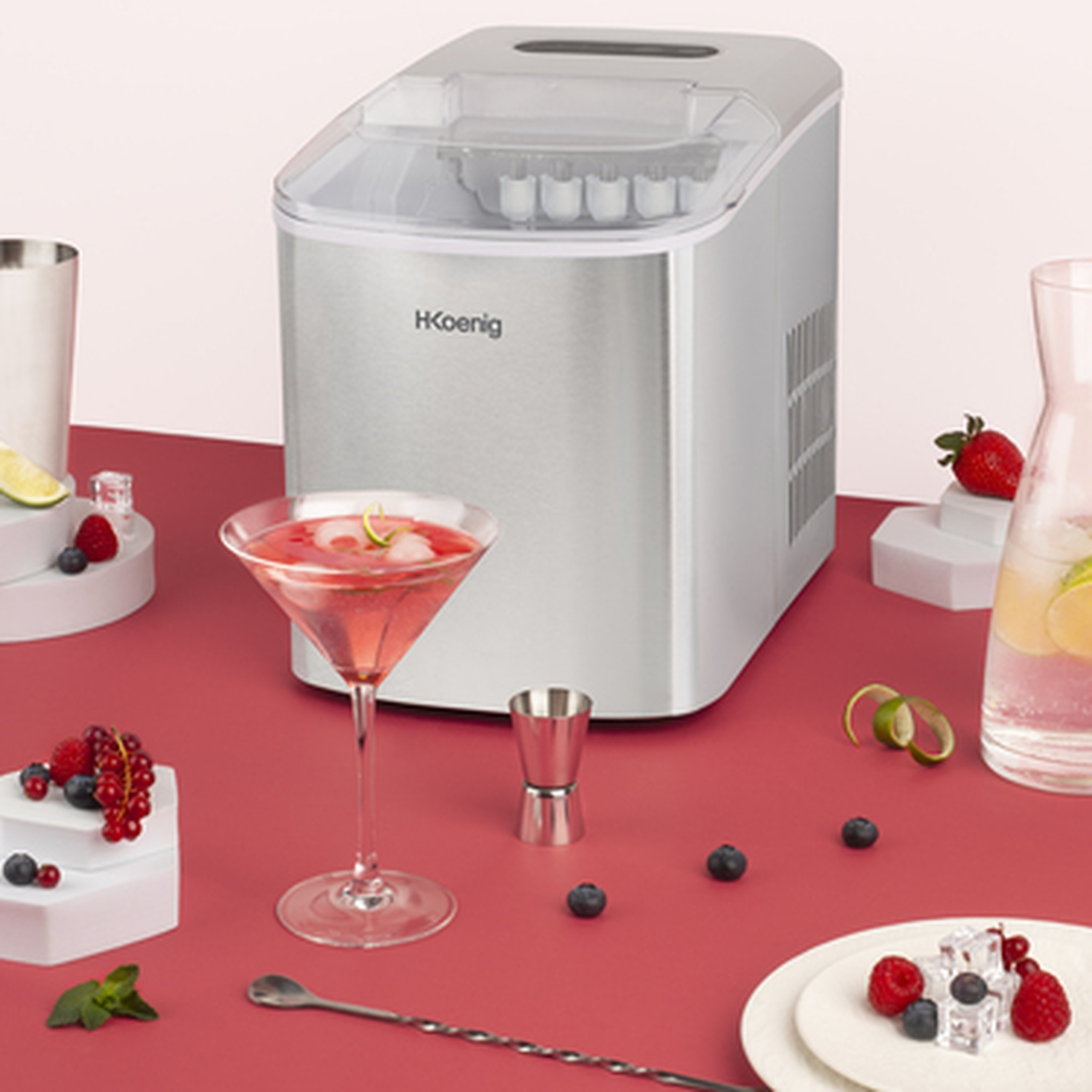 Macchina per il ghiaccio con cocktail, frutti di bosco e caraffa su tavolo rosso.
