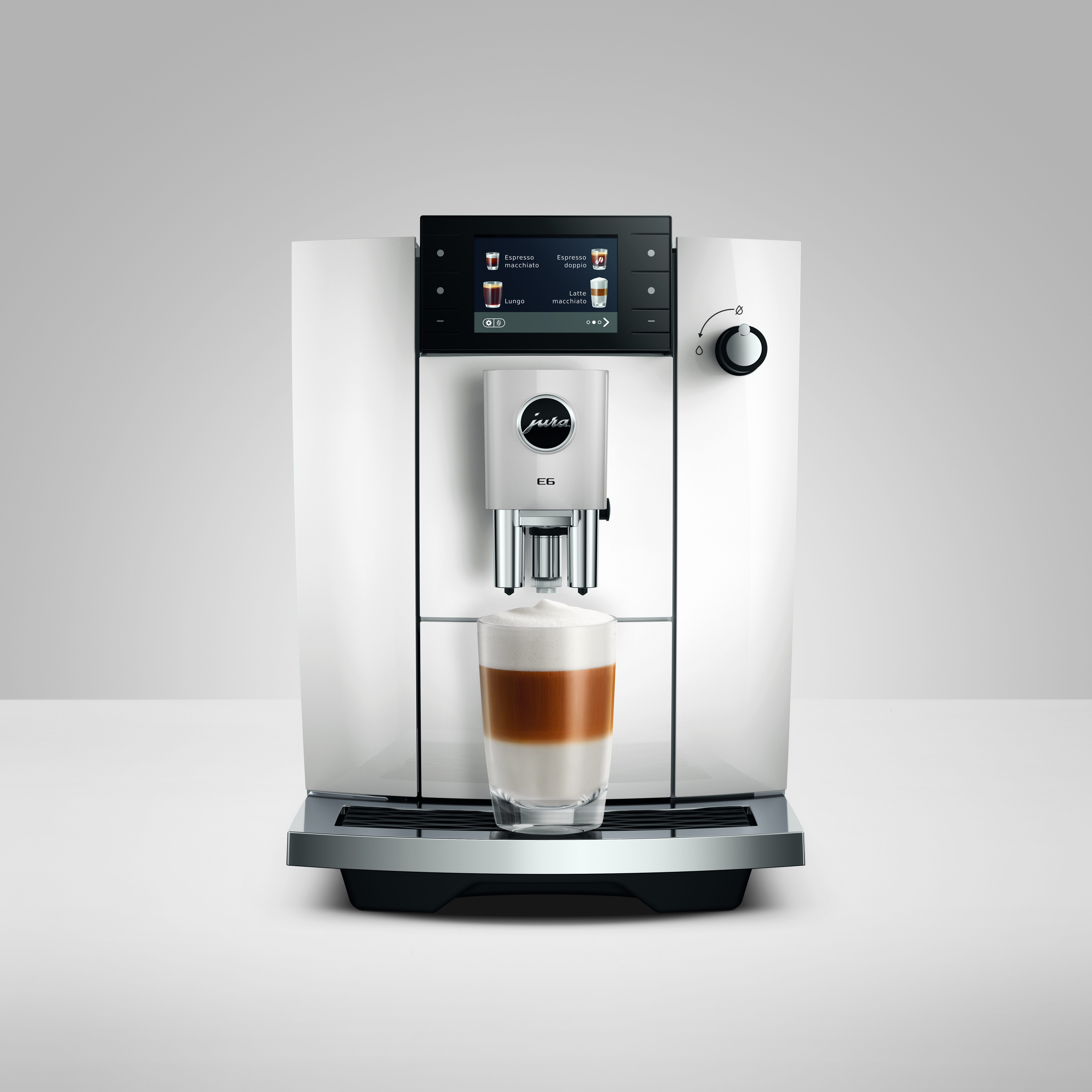 Eine weiße Kaffeemaschine brüht einen Latte Macchiato in ein Glas.