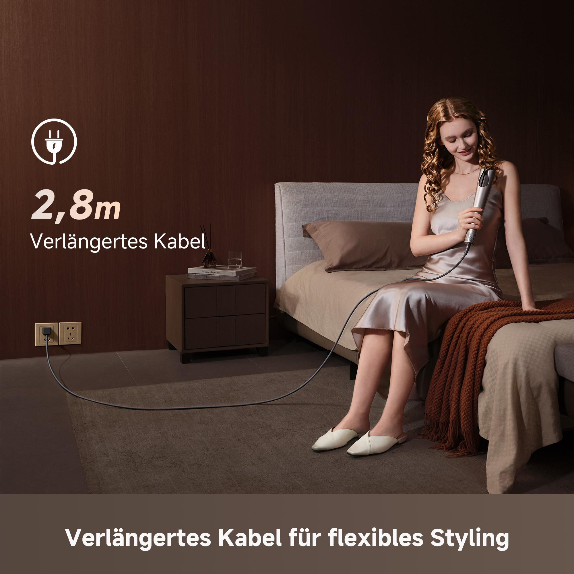 Frau sitzt auf einem Bett mit einem Lockenstab, das Kabel ist 2,8 m lang.