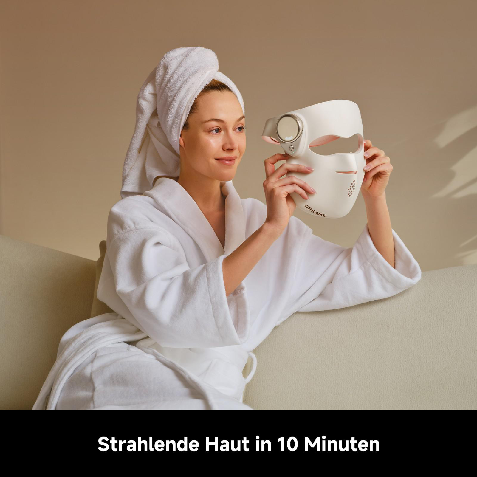 Frau im Bademantel hält eine weiße Gesichtsmaske vor ihr Gesicht.