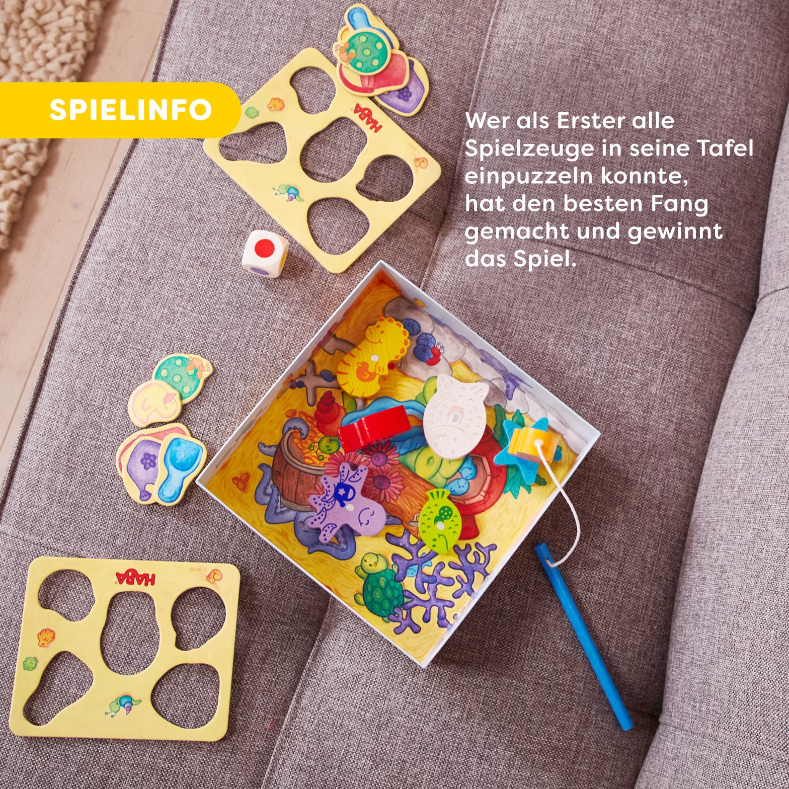 HABA játékkészlet kirakós darabokkal, kockával és játéktáblával szürke kanapén.
