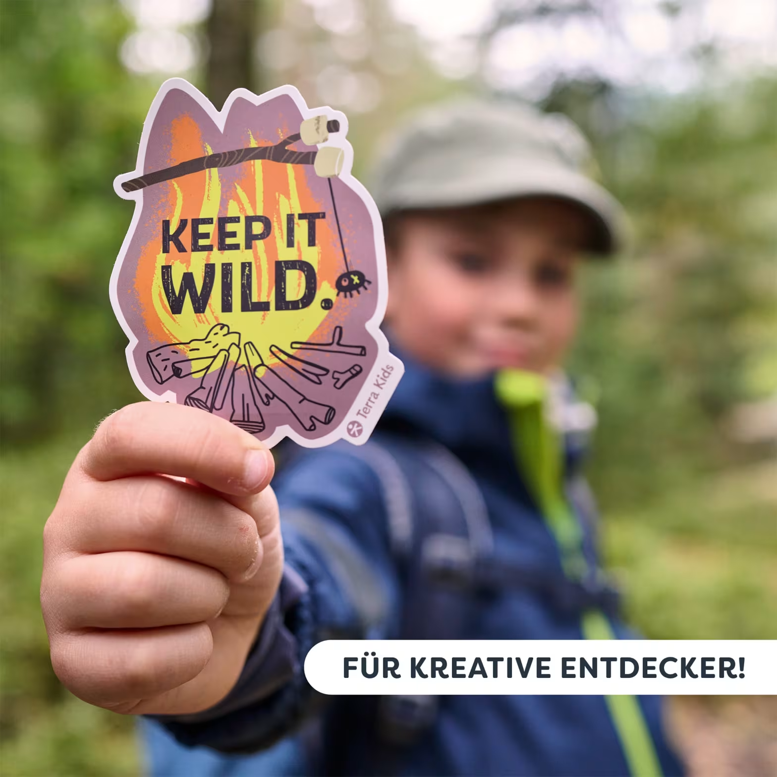 Egy gyerek egy "KEEP IT WILD" feliratú tábortűz matricát tart.