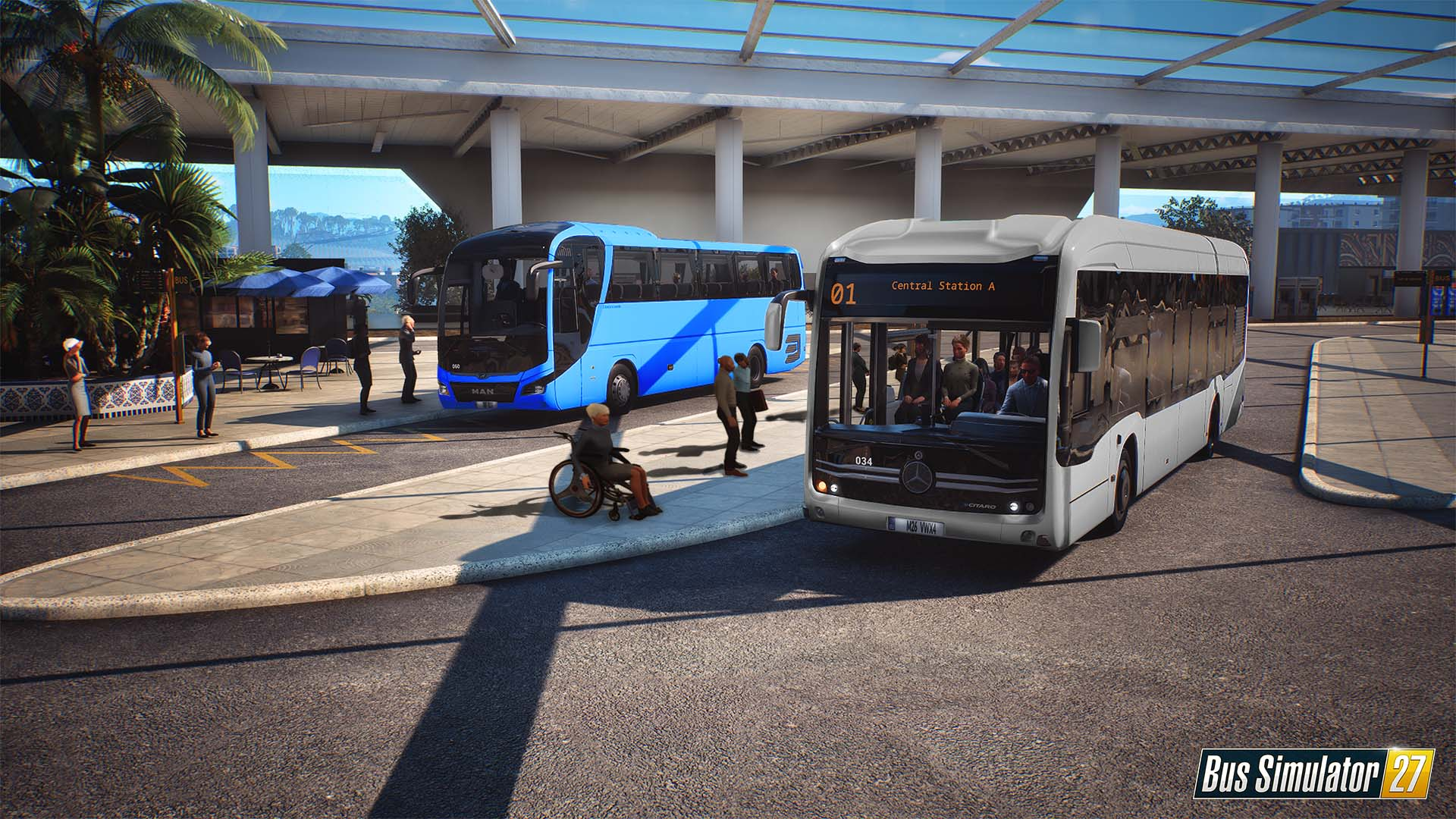 Autobuses en una estación: un autobús azul, un autobús blanco, personas y un hombre en silla de ruedas.