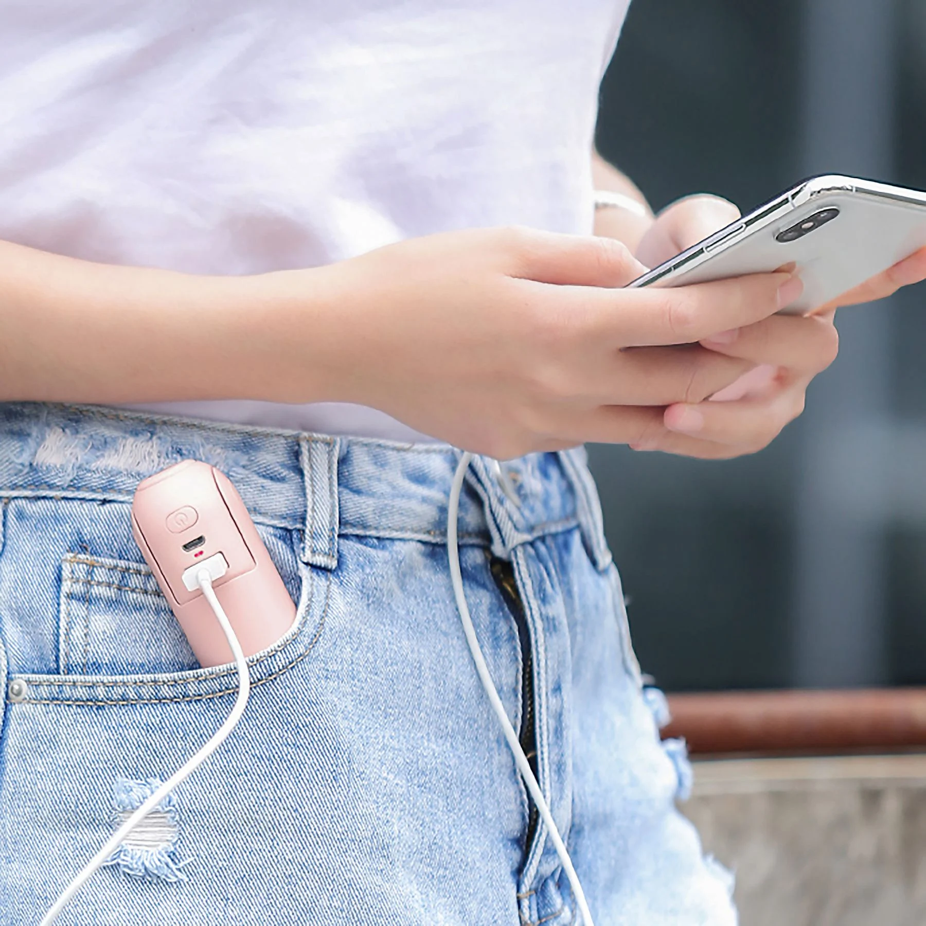 Una persona usa un móvil con un cargador rosa en el bolsillo de sus vaqueros.