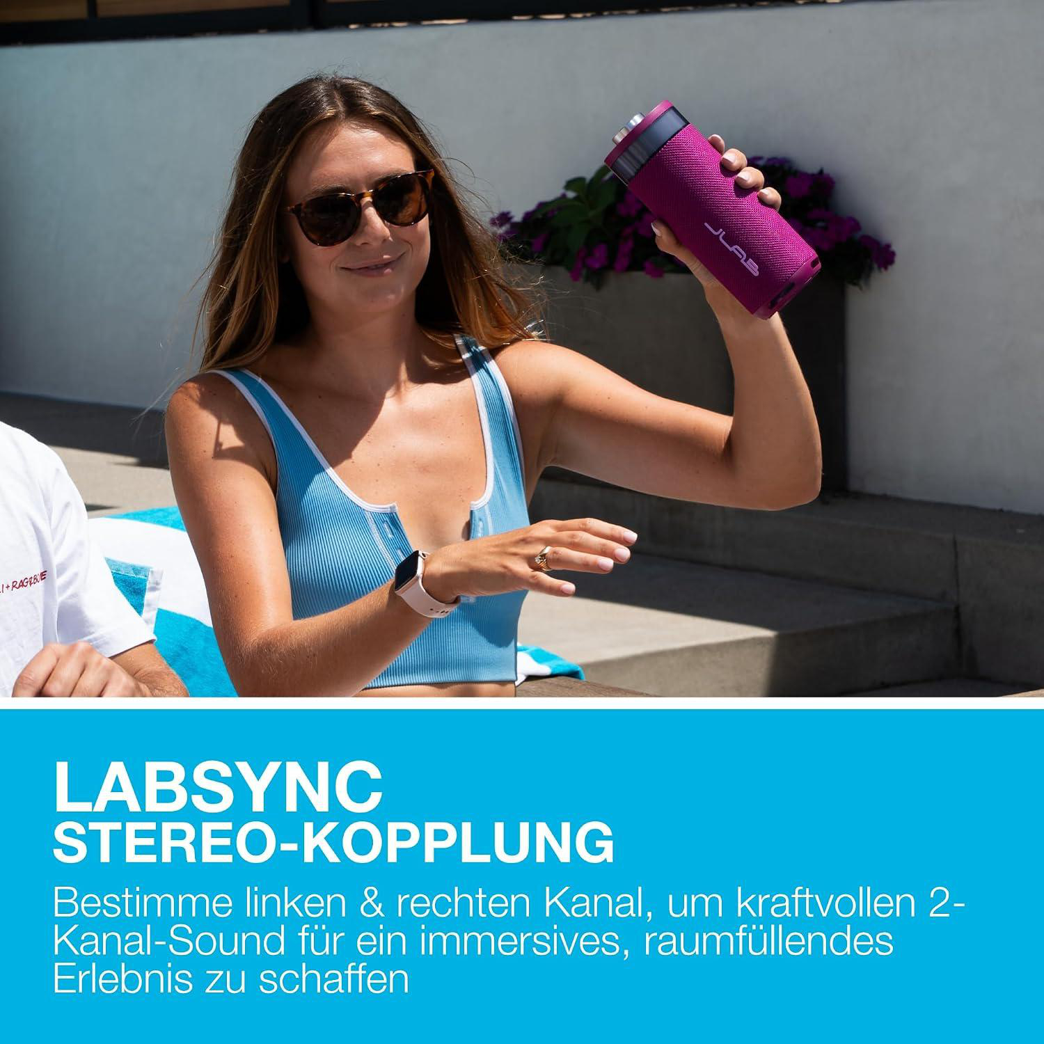 Eine Frau hält einen lila Lautsprecher in der Hand, mit einem Mann im Hintergrund.