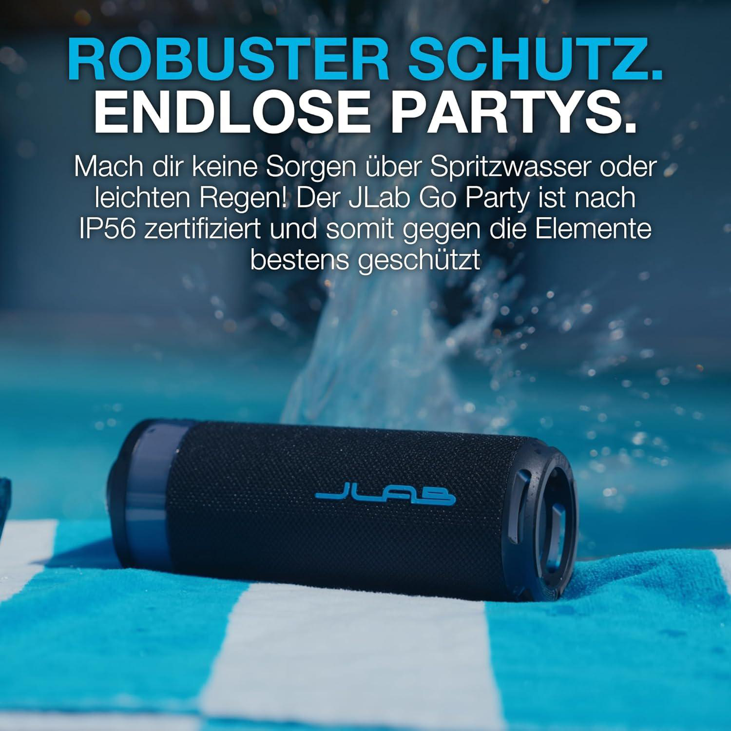Ein blauer JLab Go Party Lautsprecher auf einem Handtuch, mit Wasserfontänen.
