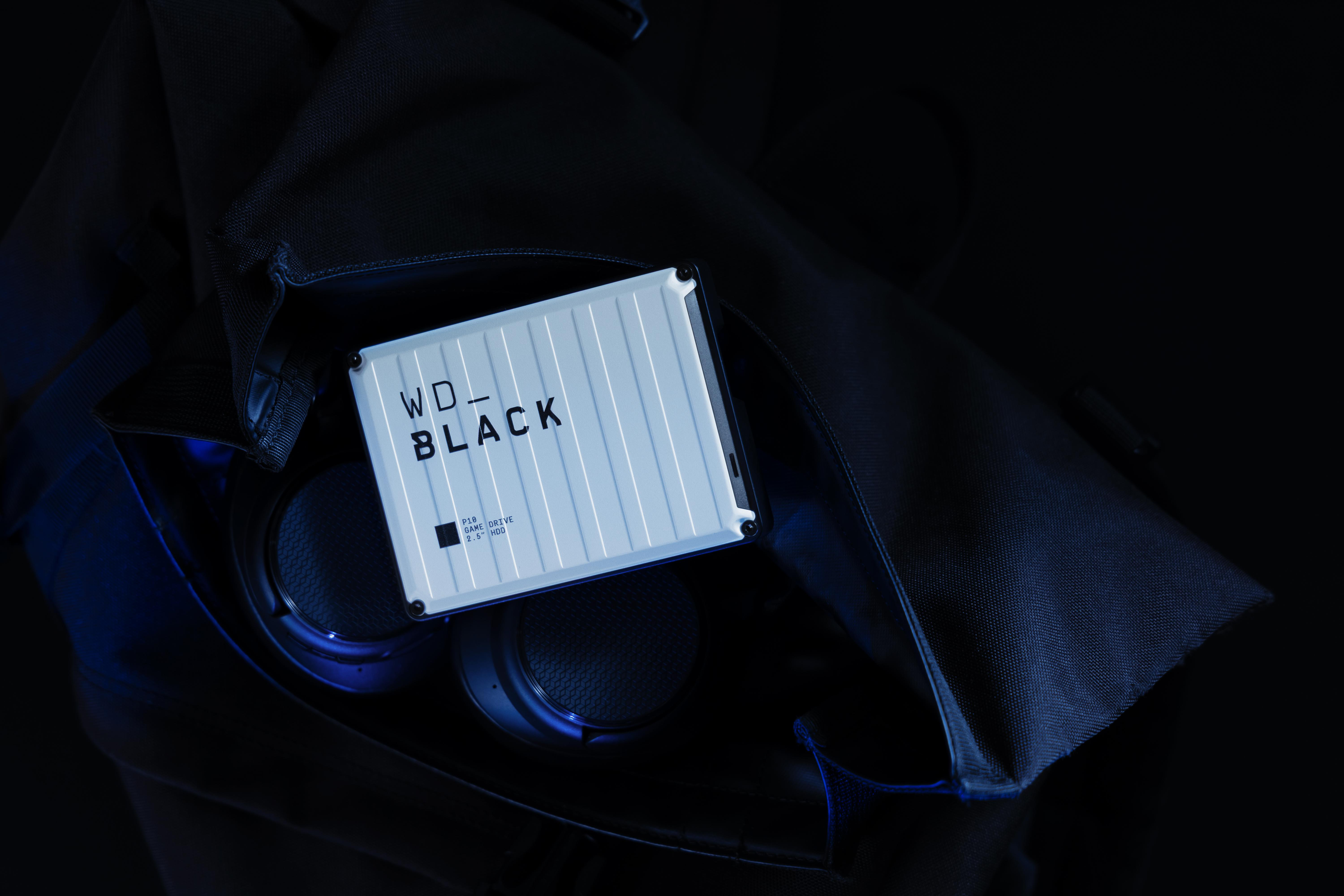 Eine weiße WD_BLACK P10 Game Drive liegt auf schwarzem Stoff, mit blauem Licht auf Kopfhörern.