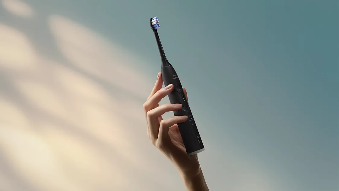 Egy kéz fekete elektromos fogkefét tart kék és fehér sörtékkel.