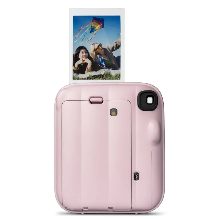 Rosa Sofortbildkamera mit einem Foto von zwei Frauen und einem bunten Drachen im Himmel.
