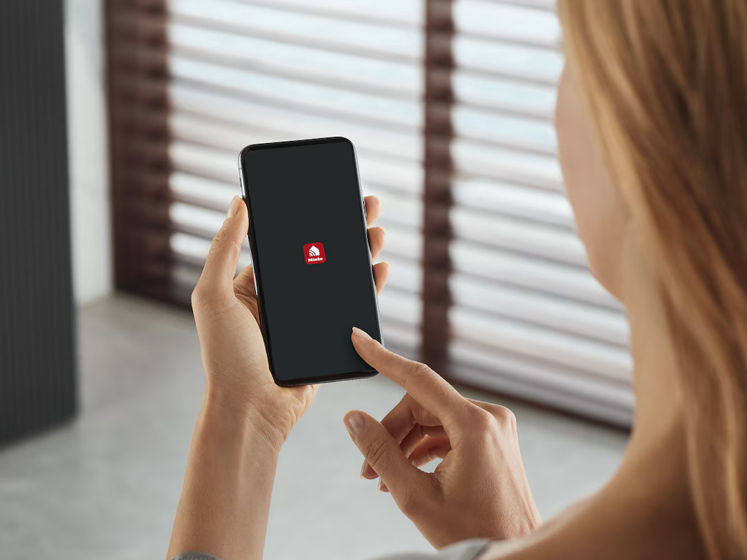 Kobieta trzyma smartfon z logo Miele. Palec dotyka ekranu.