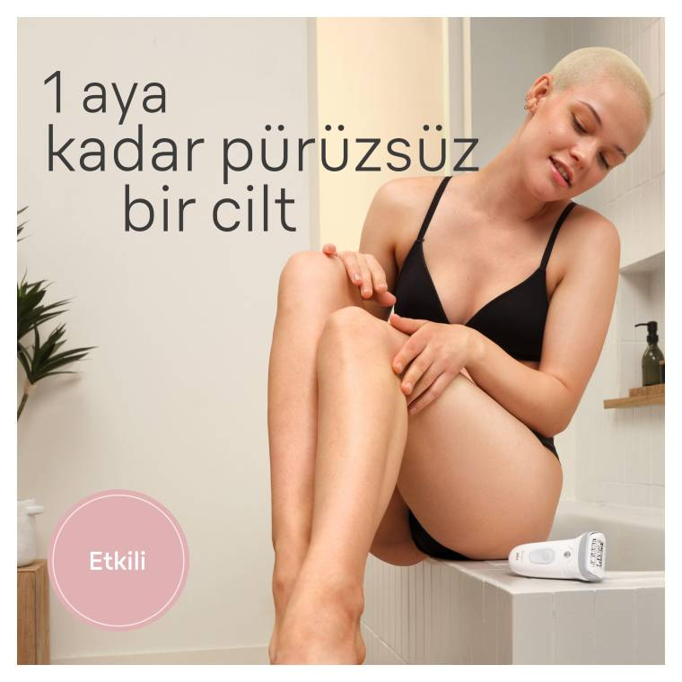 Kısa saçlı bir kadın banyoda oturuyor, bacağına dokunuyor. Yakınında epilatör var.