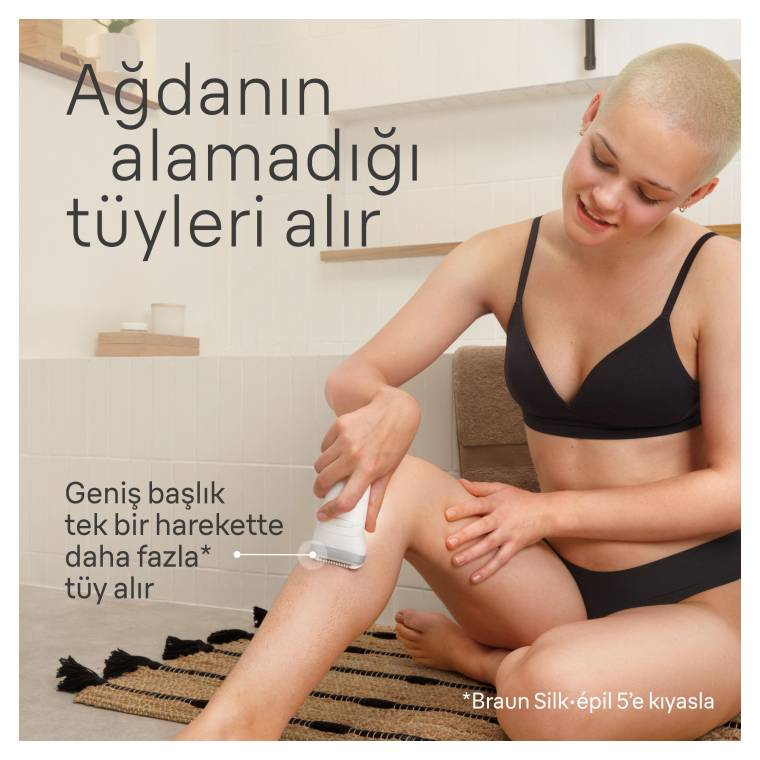 Kısa saçlı bir kadın bacağını epilatörle tıraş ediyor.