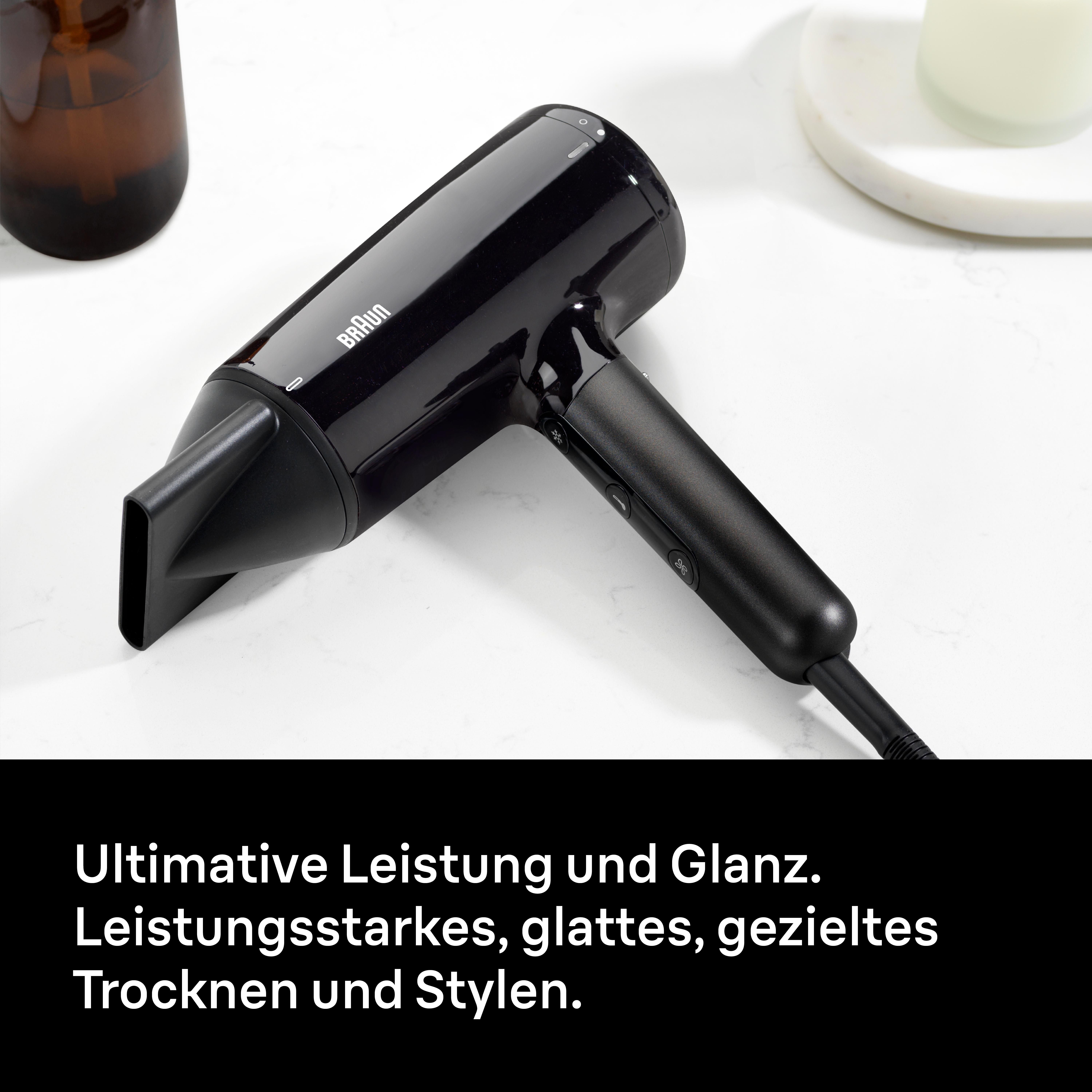 Ein schwarzer Braun Haartrockner steht auf einer Marmoroberfläche neben einem Glas.