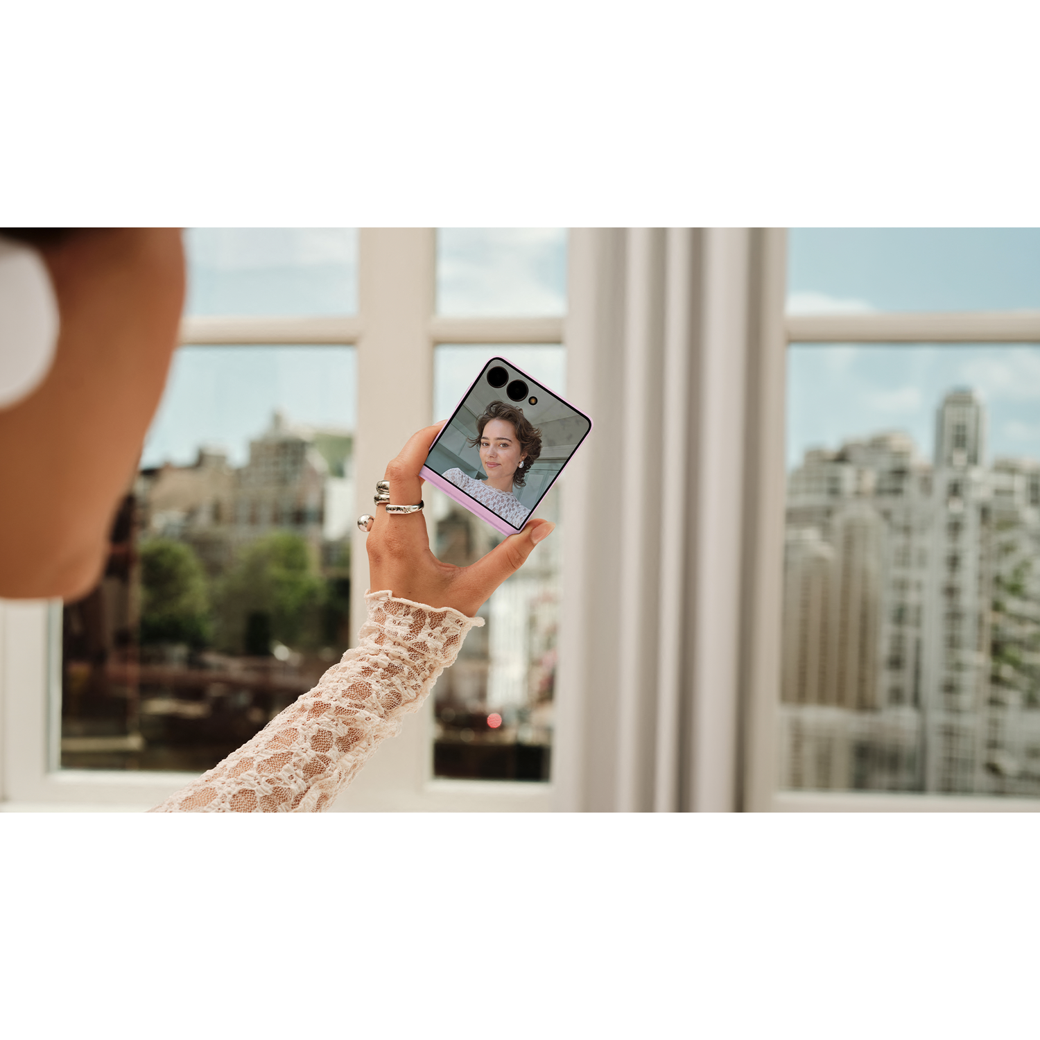 Hand met telefoon met vrouw op scherm, kanten mouw, raam met stadszicht.