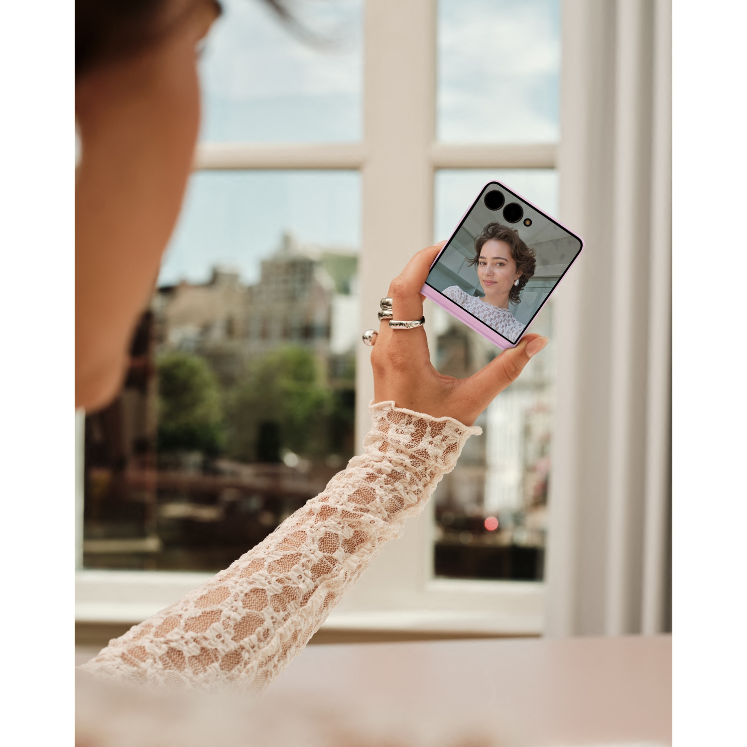 A woman holds a smartphone displaying a portrait on its screen.