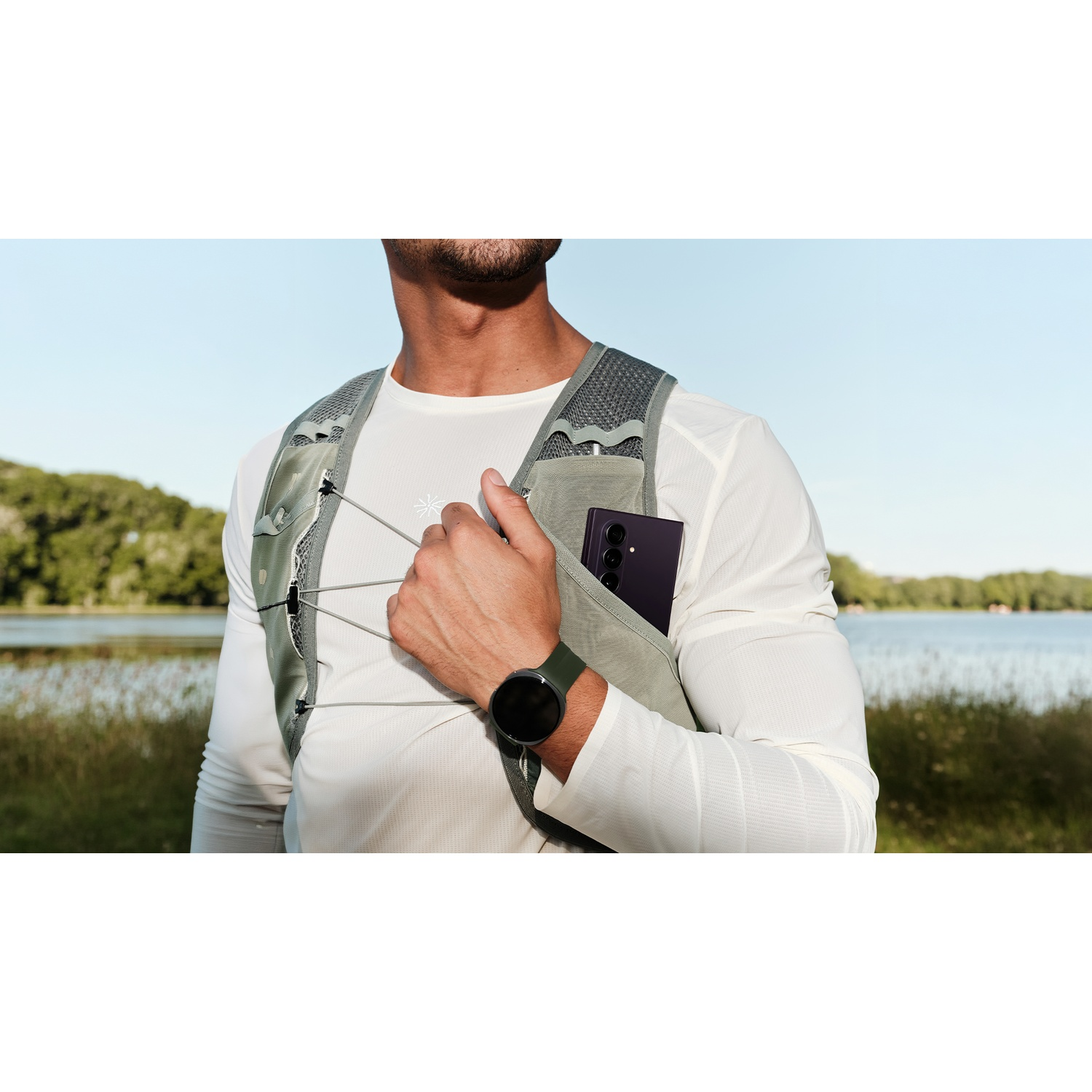 Man wearing a vest, phone in pocket, watch on arm, lake in background.