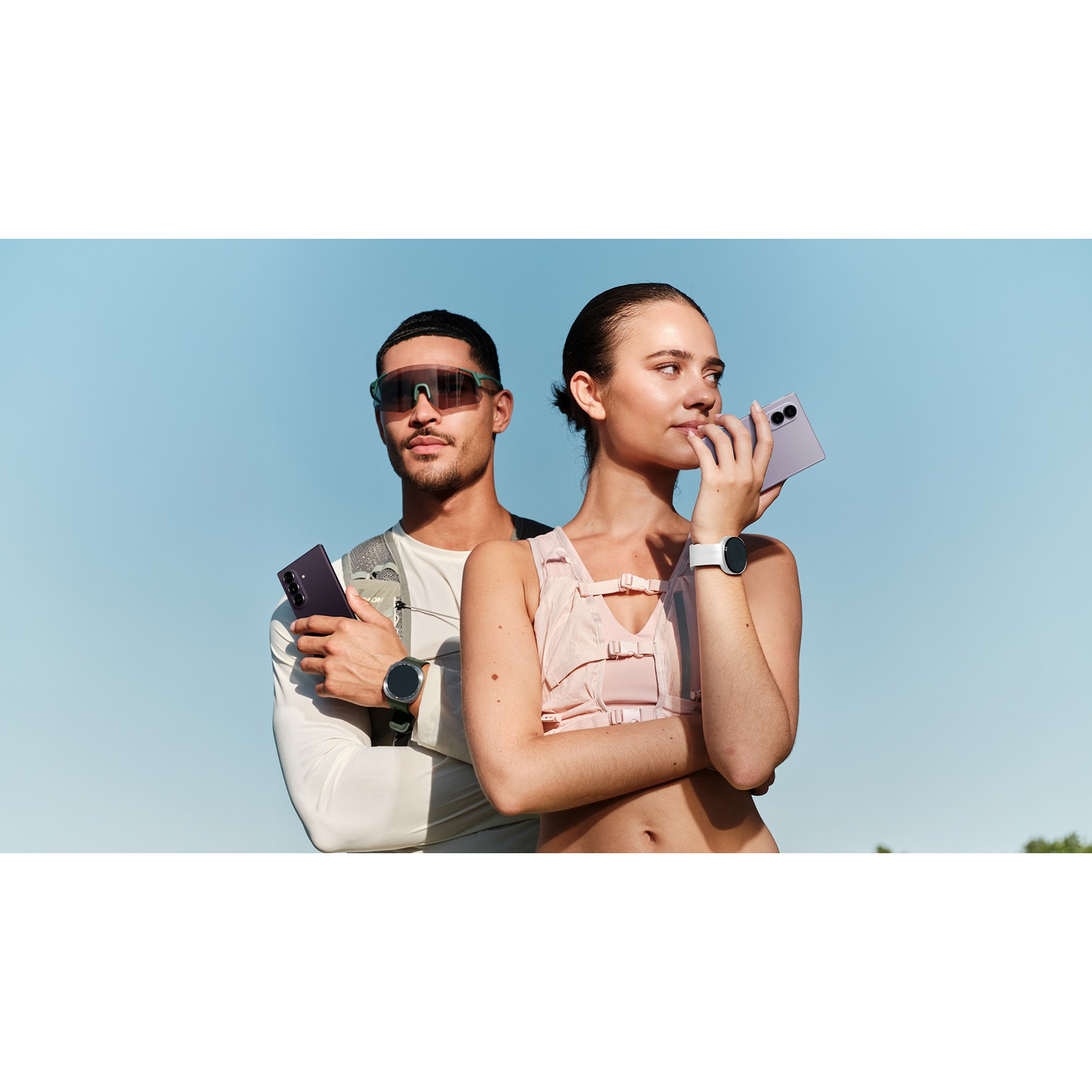 Man and woman holding smartphones and wearing watches against blue sky.