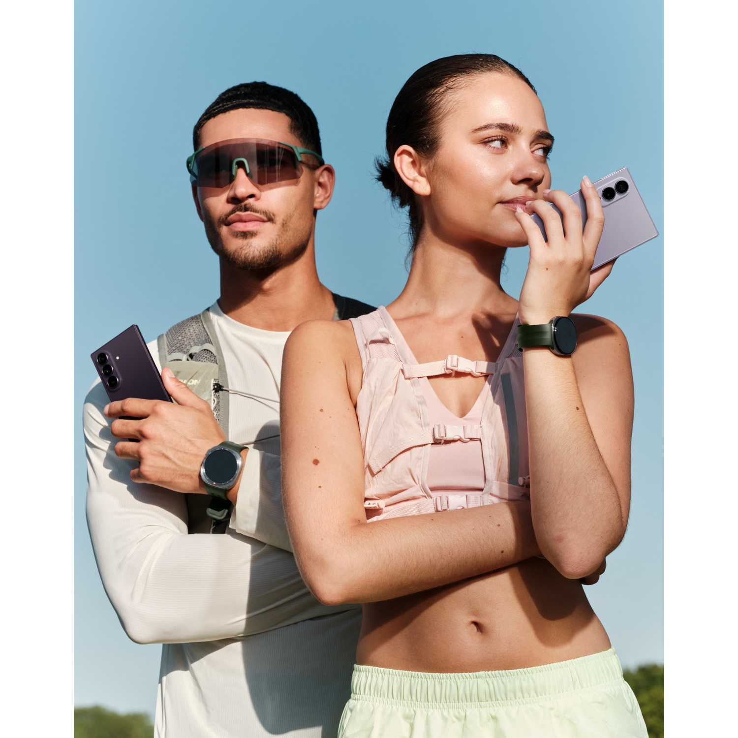 Man with sunglasses and woman hold purple phones, blue sky backdrop.
