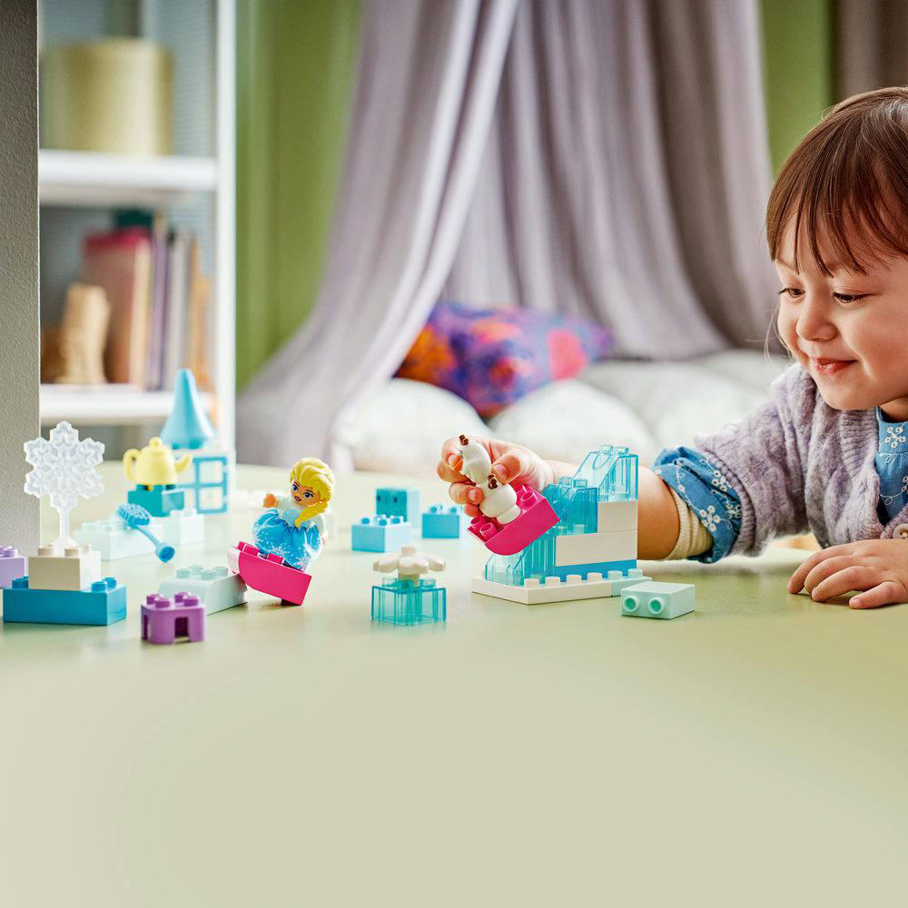 Ein kleines Mädchen spielt mit bunten Bausteinen und Figuren auf einem Tisch.