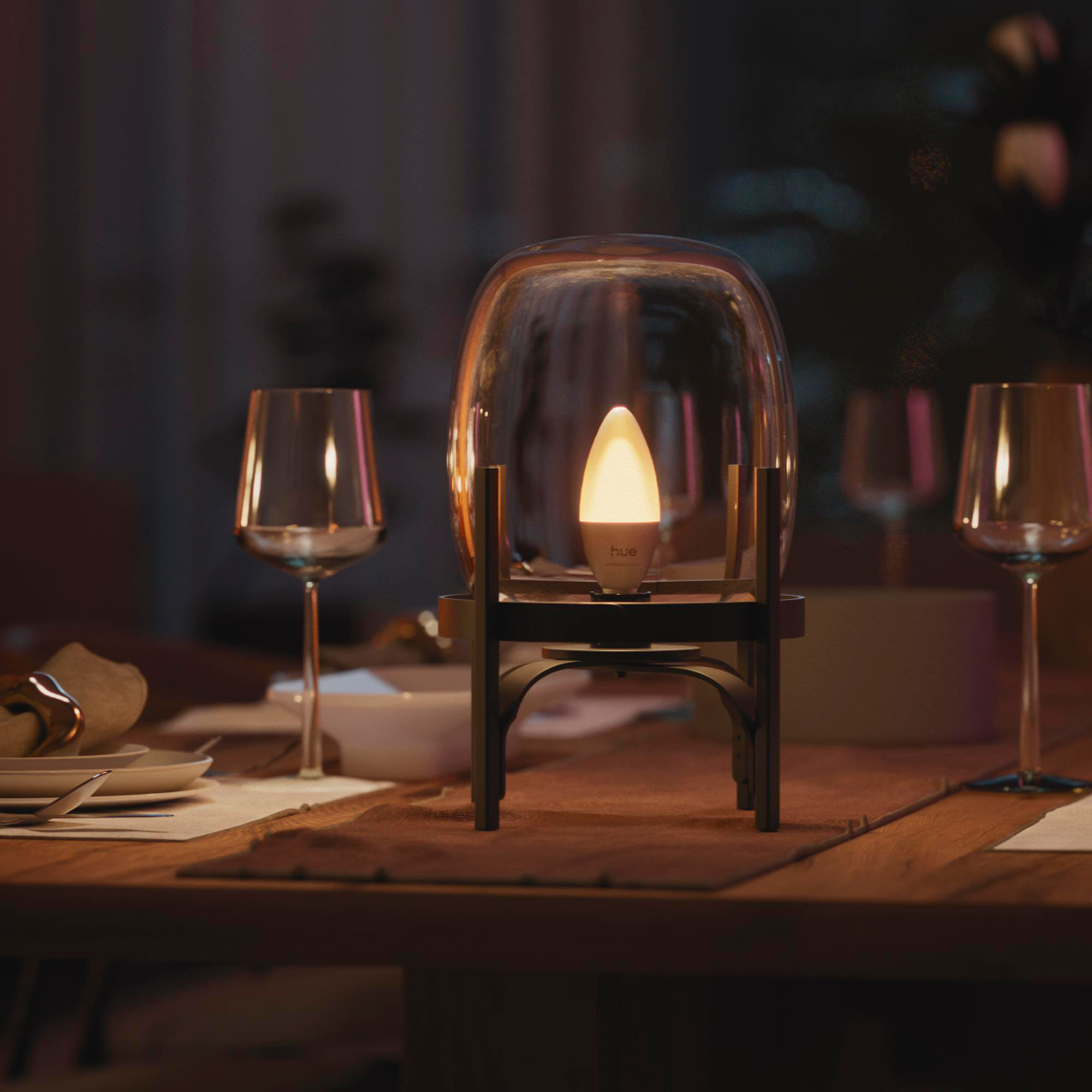 Ein beleuchteter Kerzenlicht-LED-Glühbirne in einem Glasständer auf einem Esstisch.