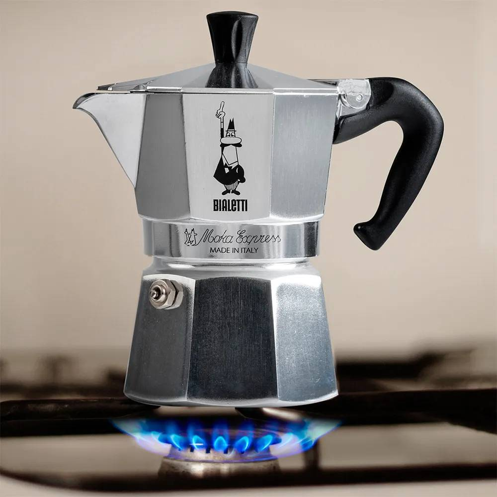 Cafetera Bialetti Moka Express plateada sobre cocina de gas con llamas azules.