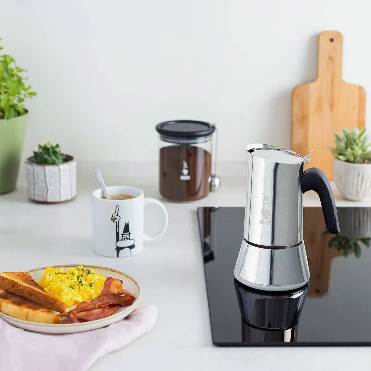 Mesa de desayuno con tostadas, huevos revueltos, tocino y cafetera.